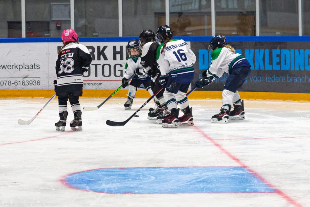 Jeugdspelers van Dordrecht Lions en de tegenstander strijden om de puck langs de boarding tijdens de U9- en U11-wedstrijddag in de Sportboulevard.