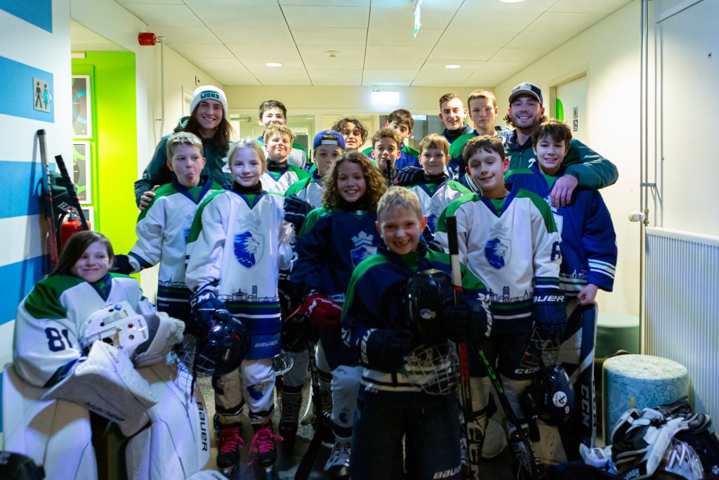 Jeugdspelers van Dordrecht Lions poseren samen in de gang van de ijsbaan, volledig in uitrusting en klaar voor hun demonstratie