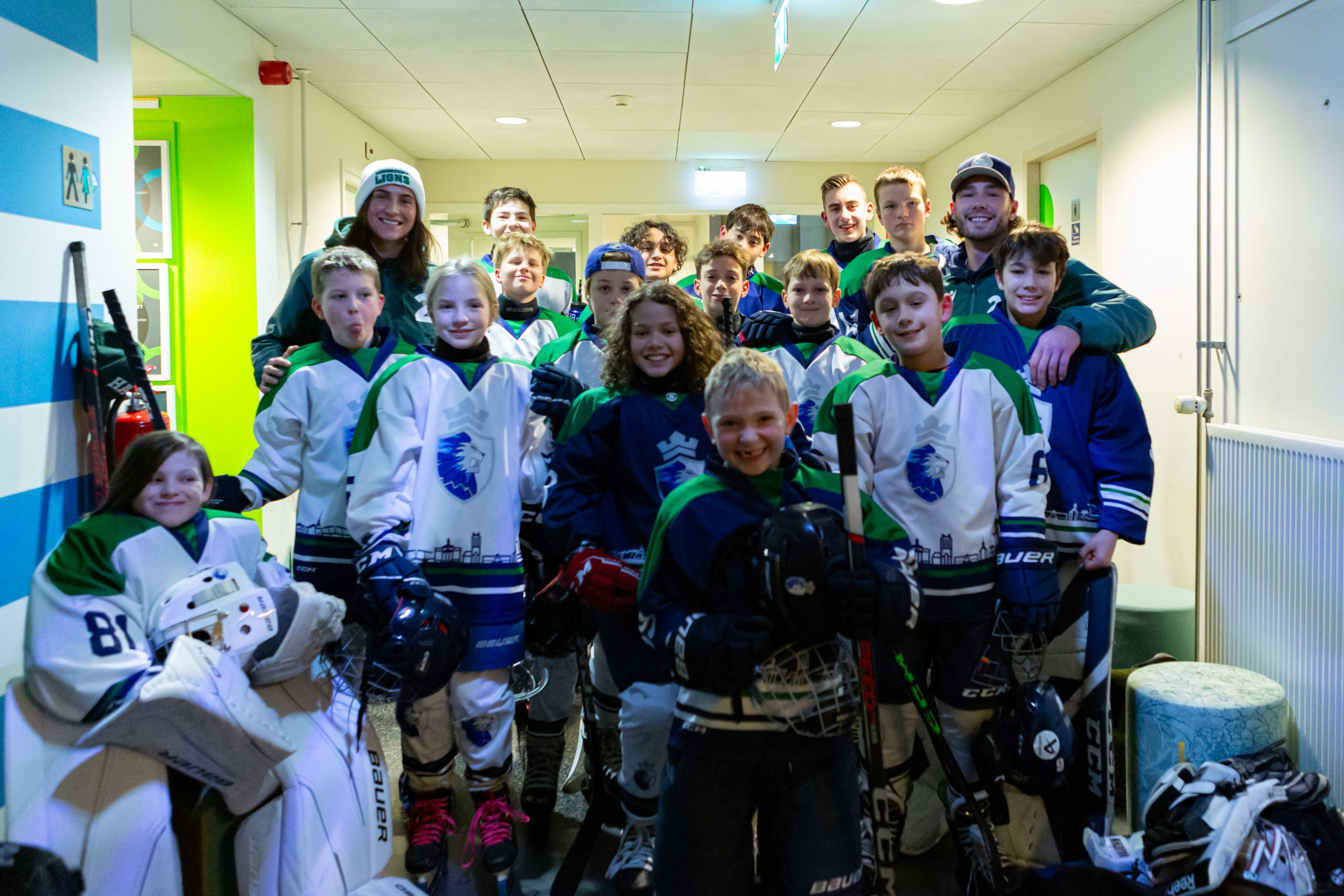 Jeugdspelers van Dordrecht Lions poseren samen in de gang van de ijsbaan, volledig in uitrusting en klaar voor hun demonstratie