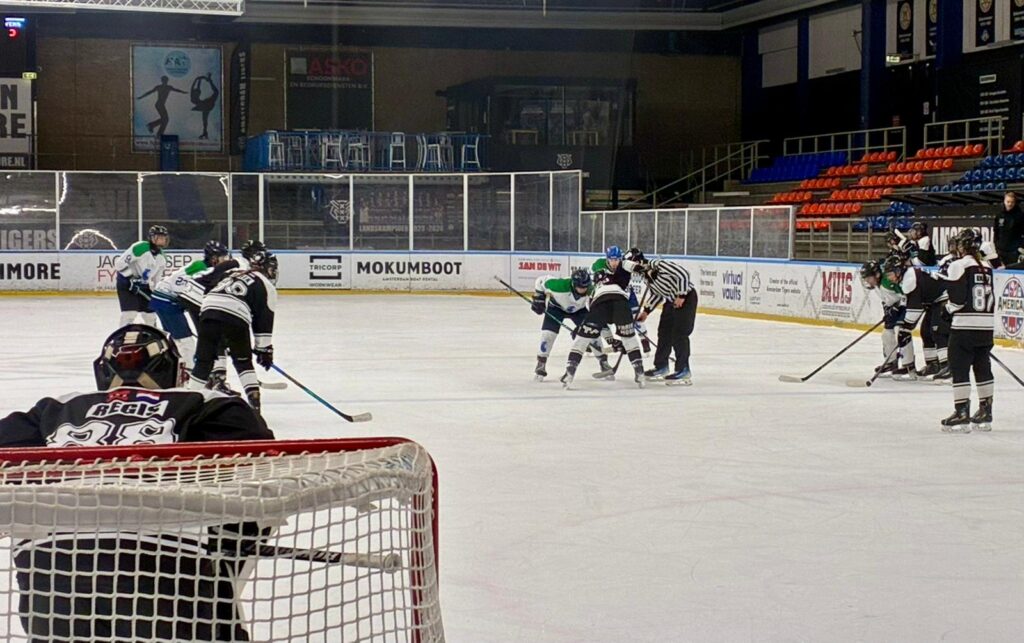 Face-off tussen Dordrecht Lions U17 en Amsterdam Tigers U17 in de Jaap Edenhal, gefotografeerd vanaf achter het doel.
