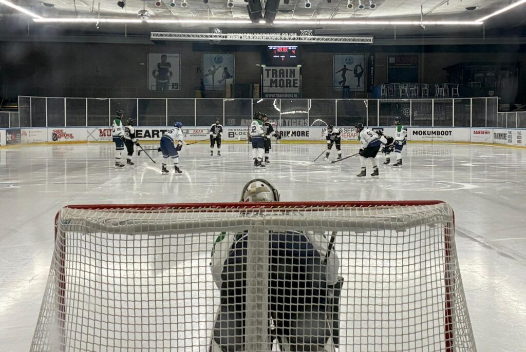 Dordrecht Lions U17 in actie tegen Amsterdam Tigers U17 in de Jaap Edenhal, gezien vanaf achter het doel tijdens een face-off.